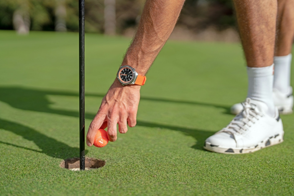 Golfer wearing fancy watch retrieves ball from hole on green. Cannabis use is accepted by affluent people. 