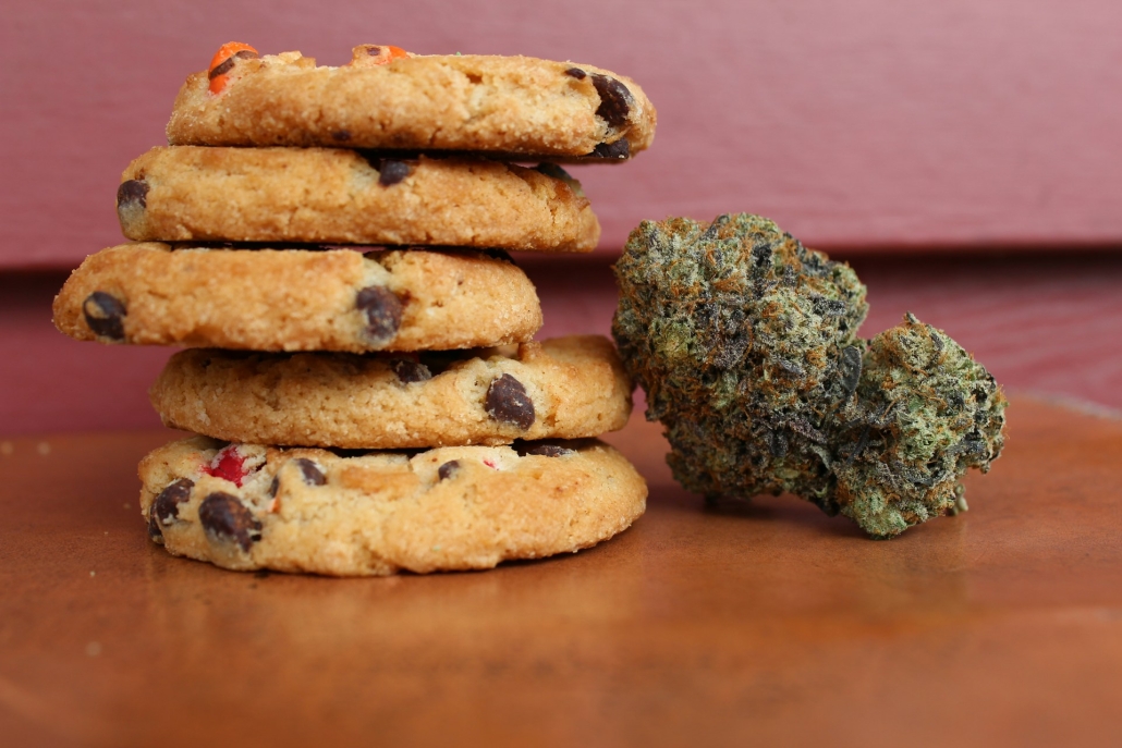 Five chocolate chip cookies made with cannabis-infused butter beside cannabis buds. How to Make Cannabis-Infused Butter: A Simple Recipe - Earthy Select