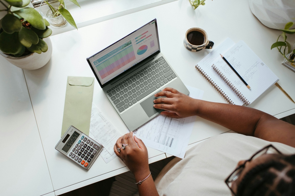 Person working at a laptop. Calculator, paperwork, coffee and a potted plant are on the desk. Microdosing THC is related to finding a perfect balance in life